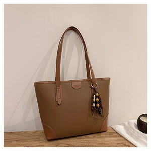 Detailed view of brown lychee grain leather tote bag with wooden bead charm on a wooden table