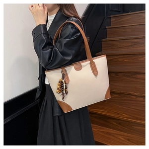 Detail of cream-colored lychee leather tote bag with brown trim and wooden bead tassel