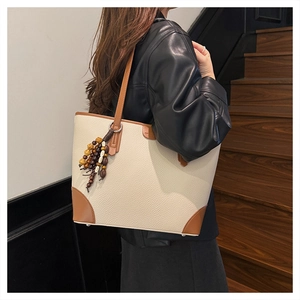 Detail of cream white pebbled tote bag with brown leather corners and ethnic beads