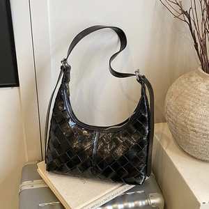Schwarze gewebte Hobo-Tasche aus Leder auf einem silbernen Koffer in minimalistischem Stil