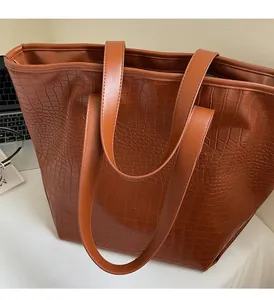 Detail view of the brown tote bag featuring embossed crocodile texture and wide handles