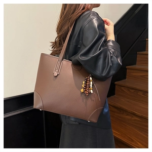 Detail of deep brown pebble leather tote bag with vintage beaded charm and shoulder straps