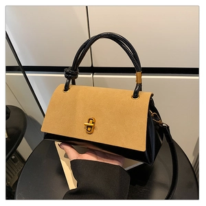 Detail of minimalist two-tone handbag with camel suede flap and gold twist lock closure