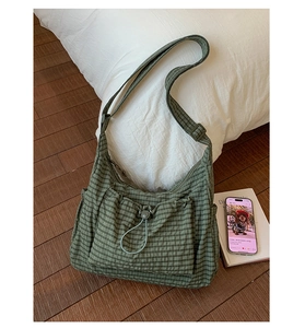 Détail du sac bandoulière à carreaux verts avec poche à cordon sur literie blanche