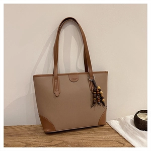 Close-up of contrast leather tote with wooden bead charm and embossed fashion logo