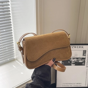 Retro brown saddle bag in leather and suede mix held against artistic light and shadow