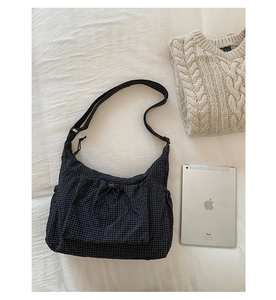 Vue à plat d'un sac bandoulière en toile à carreaux noirs avec iPad sur un lit blanc
