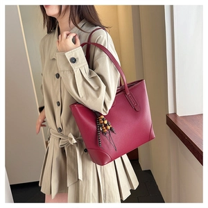 Detailed view of dark red lychee grain leather tote bag with wooden bead tassel charm