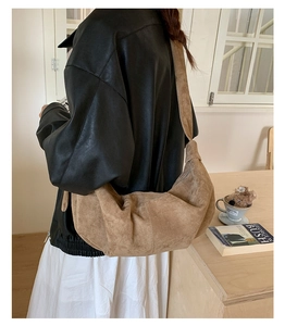 Brown suede crescent bag detail on a model in a cozy indoor lifestyle setting
