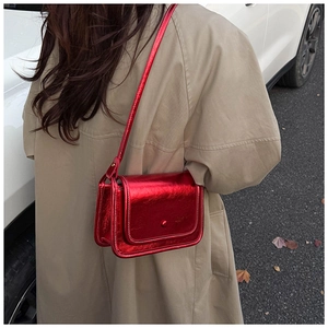 Outdoor shot of a red metallic crossbody bag with a flap cover and a slim shoulder strap