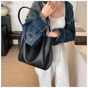 Grand sac fourre-tout en cuir noir porté à l'épaule dans un intérieur moderne