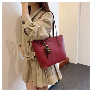 Detail of burgundy leather tote bag with lychee texture and colorful wood bead tassel