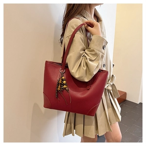 Close-up of wine red litchi leather tote bag with wooden bead tassel on a model