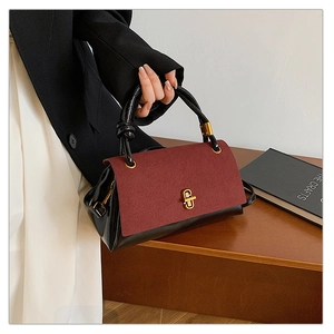 Detail of burgundy suede and black patent leather patchwork handbag with gold clasp
