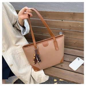 Detail view of large khaki tote bag with caramel leather trim and colorful bead tassel