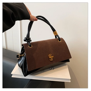 Detail of two-tone handbag showing brown suede flap, black leather and gold twist lock