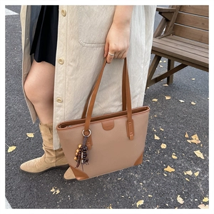 Macro view of textured brown leather tote bag with ethnic wooden bead charm detail