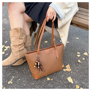Close-up of deep brown lychee texture tote bag with wood bead tassel in autumn setting