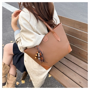 Close-up of brown pebbled leather tote bag with vintage tassel and wood bead charm