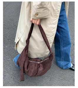 Detail of a dark brown suede hobo bag featuring a knotted shoulder strap and silver metal zipper