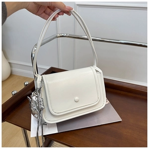 Detail of white leather shoulder bag with a silver cat charm and round buckle closure