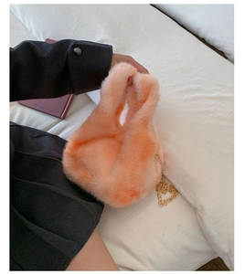 Detail of soft peach plush faux fur texture with elegant gold chain strap handbag