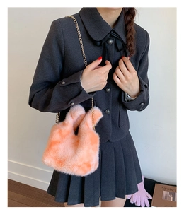 Detail showing plush faux fur texture and gold chain strap of the orange handbag