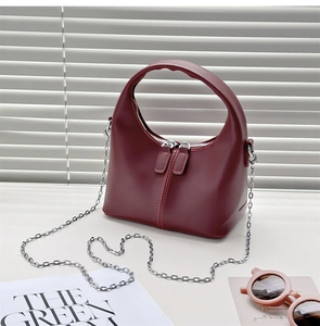 Detail of burgundy half-moon handbag with dual zippers, silver chain and fashion props