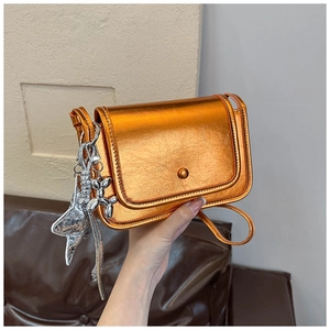 Detail of metallic orange mini flap bag featuring a silver balloon dog charm decoration