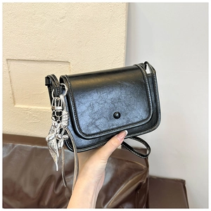 Detail of black crossbody bag with white stitching and silver rabbit pendant