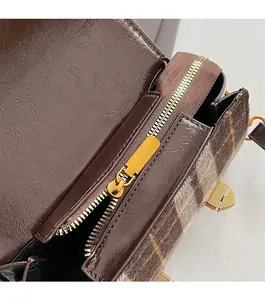 Détail de la fermeture éclair dorée et tissu à carreaux sur le sac bandoulière en cuir