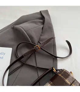 Détail de la bandoulière en cuir marron réglable avec boucle dorée sur un sac vintage à carreaux