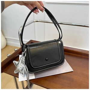 Detailed view of black crossbody bag with white stitching and silver star charm