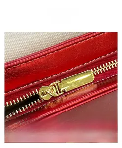 Detail of red leather crossbody bag featuring gold zipper and polished metal hardware