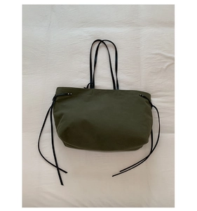 Detail of olive green canvas tote bag with black leather straps and side drawstrings