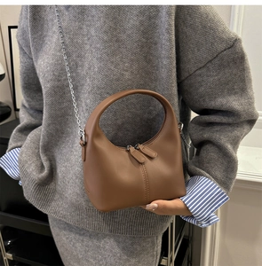 Brown leather crescent bag with silver chain strap worn by model in casual style