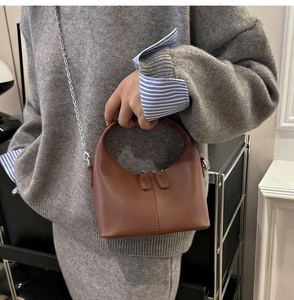 Detail of a brown leather crossbody bag with silver chain and dual zipper closure