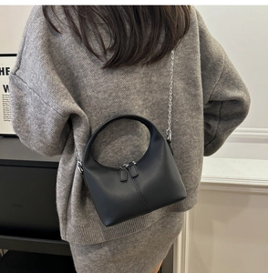 Detail of a black matte crossbody bag with silver zippers and chain strap on a model