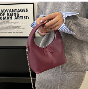 Detail of burgundy leather handbag with dual zippers and a detachable silver chain strap