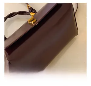 Detailed close-up of dark red glossy leather texture and gold metal buckle on shoulder bag