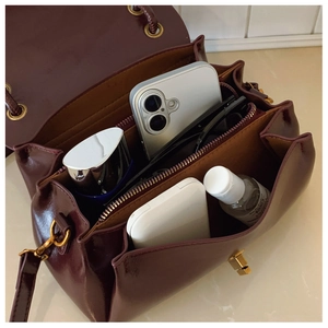 Detailed interior of glossy burgundy shoulder bag showing compartments and golden hardware