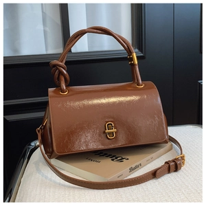 Detail of dark brown glossy leather handbag featuring a unique knotted handle and gold lock