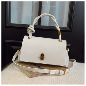 Detail of creamy white patent leather handbag with gold twist lock and knotted handle