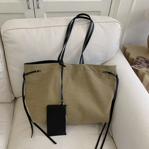 Minimalist khaki canvas tote bag with black straps and small pouch on fabric sofa