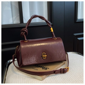 Detail of burgundy glossy leather bag with gold twist lock and knotted handle texture