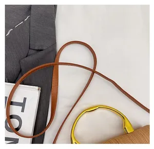 Detail of a woven handbag featuring a thin brown leather strap and golden metal handle