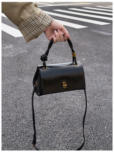Detail of black glossy leather handbag featuring vintage gold twist lock and knot handle