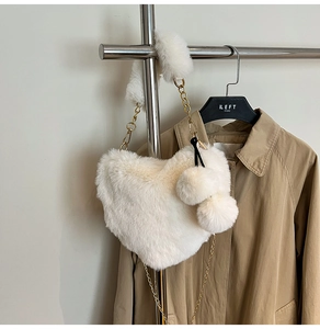 Detail der herzförmigen Kunstpelz-Tasche in Cremeweiß mit Goldkette und Bommel-Anhängern