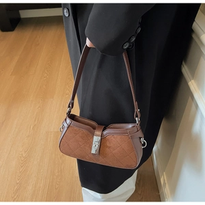 Close-up of brown quilted faux suede baguette bag with silver twist lock on black coat