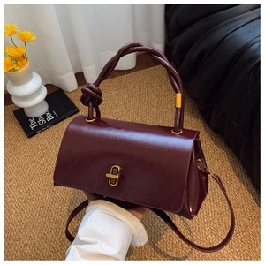 Detail of burgundy glossy leather handbag featuring braided handle and gold twist lock